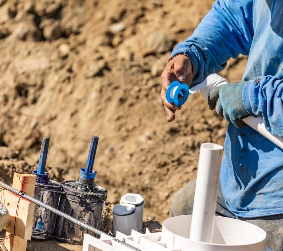 Plumber Applying PTFE Tape To PVC Pipe At Construction Site.